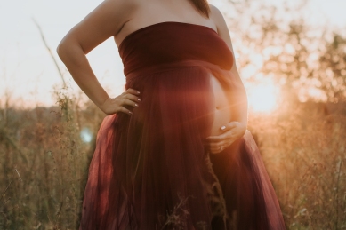 Maternity shoot at sunset in field with red maternity open belly dress.
